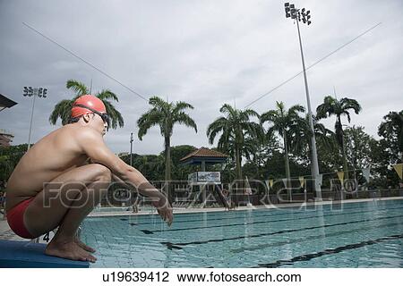 Stock Image - Side profile of a young man squatting on a starting block. Fotosearch