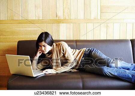Close-up of a young woman lying on a couch in front of a laptop View Large Photo Image Stock Image - Close-up of a young woman lying on a couch in front of a laptop. Fotosearch