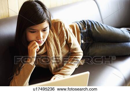 Stock Photograph - Close-up of a young woman lying on a couch in front of a laptop. Fotosearch