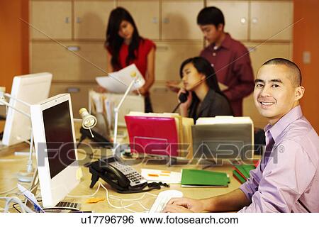 Portrait of a businessman using a computer with three business executives working in the background View Large Photo Image Stock Photograph - Portrait of a businessman using a computer with three business executives working in the background. Fotosearch