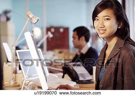 Stock Image - Portrait of a businesswoman sitting in front of a computer in an office and smiling. Fotosearch