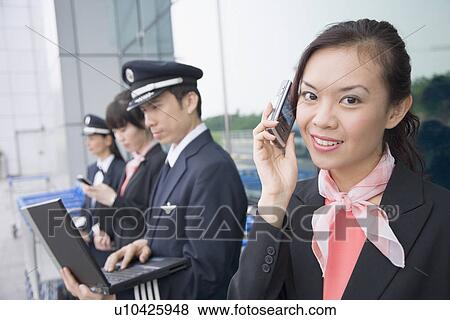 Portrait of a female cabin crew talking on a mobile phone with a pilot using a laptop in the background View Large Photo Image Stock Photo - Portrait of a female cabin crew talking on a mobile phone with a pilot using a laptop in the background. Fotosearch