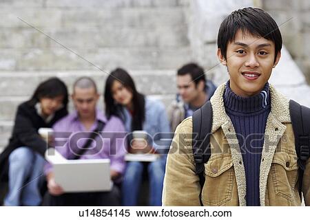 Portrait of a young man smiling with his friends sitting in the background View Large Photo Image Stock Photography - Portrait of a young man smiling with his friends sitting in the background. Fotosearch