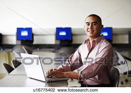 Stock Image - Portrait of a young man using a laptop and smiling. Fotosearch