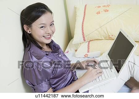 Portrait of a young woman using a laptop on the bed and smiling View Large Photo Image Stock Photo - Portrait of a young woman using a laptop on the bed and smiling. Fotosearch