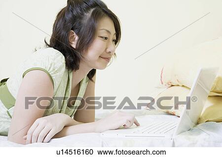 Side profile of a young woman lying on the bed and using a laptop View Large Photo Image Stock Image - Side profile of a young woman lying on the bed and using a laptop. Fotosearch