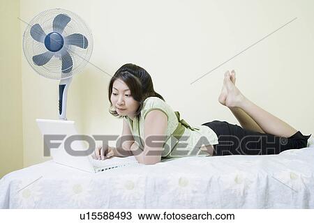 Side profile of a young woman lying on the bed and using a laptop View Large Photo Image Stock Image - Side profile of a young woman lying on the bed and using a laptop. Fotosearch