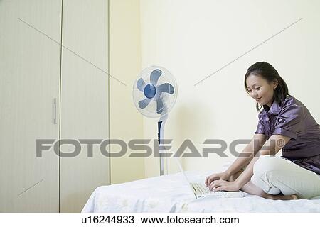 Side profile of a young woman sitting cross-legged on the bed and using a laptop View Large Photo Image Stock Image - Side profile of a young woman sitting cross-legged on the bed and using a laptop. Fotosearch