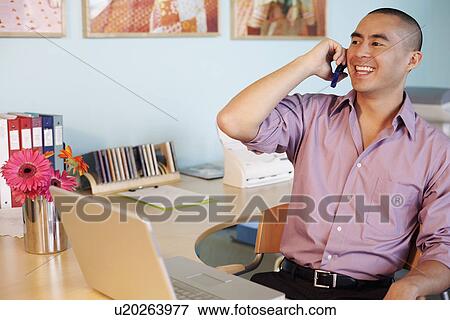 Young man talking on a mobile phone in an office and smiling View Large Photo Image Stock Photo - Young man talking on a mobile phone in an office and smiling. Fotosearch