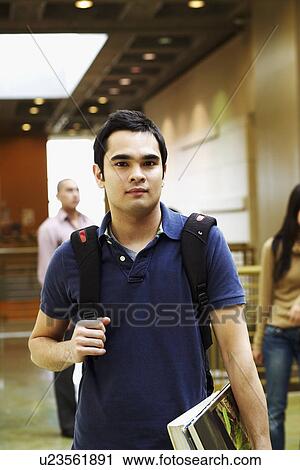 Portrait of a young man holding books and standing in the corridor View Large Photo Image Stock Image - Portrait of a young man holding books and standing in the corridor. Fotosearch