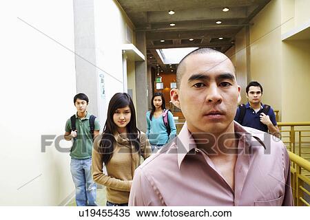 Portrait of a young man looking serious with two young women and two young men walking in the corridor behind him View Large Photo Image Stock Photography - Portrait of a young man looking serious with two young women and two young men walking in the corridor behind him. Fotosearch