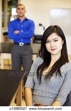 Portrait of a young woman grinning with a young man standing behind her View Large Photo Image Stock Photo - Portrait of a young woman grinning with a young man standing behind her. Fotosearch