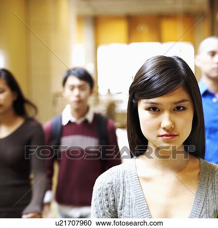Stock Image - Portrait of a young woman walking in the corridor with three people behind her. Fotosearch