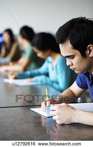 Stock Photograph - Side profile of a young man giving exams in a classroom. Fotosearch