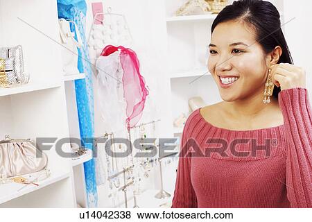 Stock Photo - Close-up of a young woman trying on an earring in a store. Fotosearch