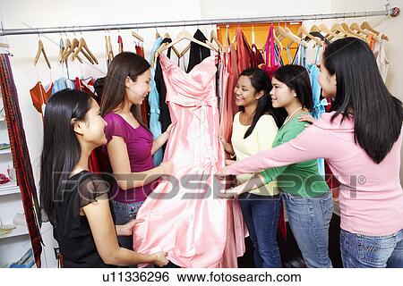 Stock Photograph - Five young women looking at a dress in a clothing store. Fotosearch