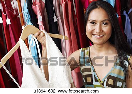 Portrait of a young woman holding a dress in a clothing store View Large Photo Image Stock Image - Portrait of a young woman holding a dress in a clothing store. Fotosearch