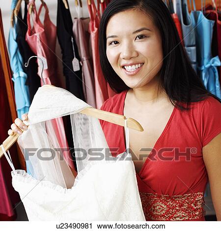 Stock Image - Portrait of a young woman holding a dress in a clothing store. Fotosearch