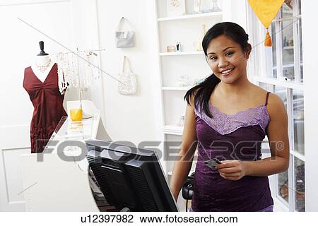 Stock Image - Portrait of a young woman standing at a checkout counter and holding a credit card. Fotosearch