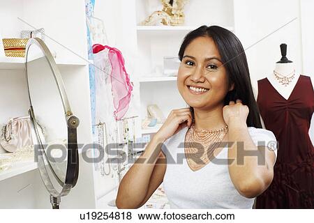 Portrait of a young woman trying on a necklace in a store View Large Photo Image Stock Photo - Portrait of a young woman trying on a necklace in a store. Fotosearch