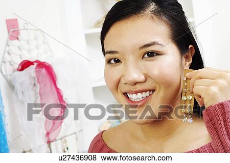 Stock Photo - Portrait of a young woman trying on an earring in a store. Fotosearch