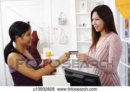 Side profile of a young woman giving a credit card to a sales clerk View Large Photo Image Stock Photo - Side profile of a young woman giving a credit card to a sales clerk. Fotosearch