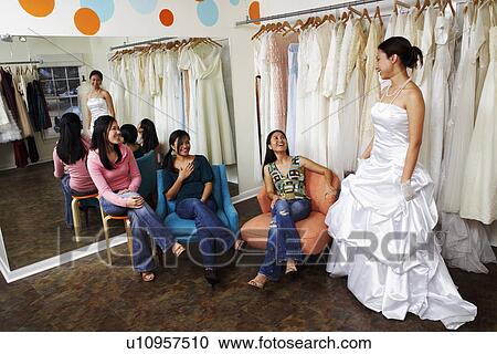 Three young women helping their friend try on a wedding dress in a bridal store View Large Photo Image Stock Image - Three young women helping their friend try on a wedding dress in a bridal store. Fotosearch