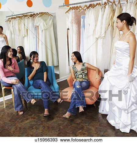 Three young women helping their friend try on a wedding dress in a bridal store View Large Photo Image Stock Image - Three young women helping their friend try on a wedding dress in a bridal store. Fotosearch