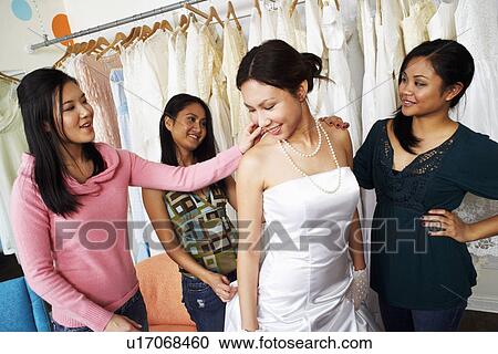 Stock Image - Three young women helping their friend try on a wedding dress in a bridal store. Fotosearch