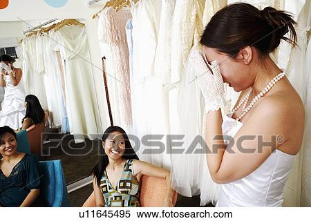 Two young women helping their friend try on a wedding dress in a bridal store View Large Photo Image Stock Photography - Two young women helping their friend try on a wedding dress in a bridal store. Fotosearch