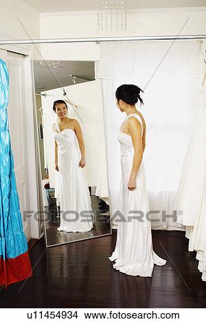 Young woman wearing a wedding dress and looking at herself in the mirror View Large Photo Image Picture - Young woman wearing a wedding dress and looking at herself in the mirror. Fotosearch