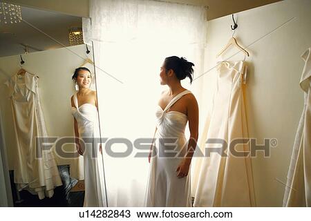 Young woman wearing a wedding dress and looking at herself in the mirror View Large Photo Image Stock Image - Young woman wearing a wedding dress and looking at herself in the mirror. Fotosearch