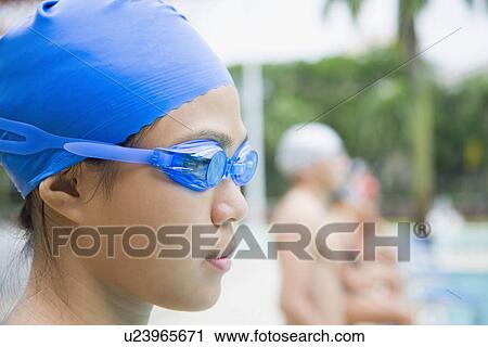 Stock Image - Close-up of a young woman wearing swimming goggles and standing at a poolside. Fotosearch
