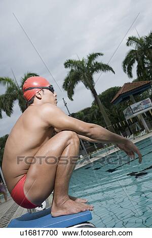 Stock Image - Side profile of a young man squatting on a starting block. Fotosearch