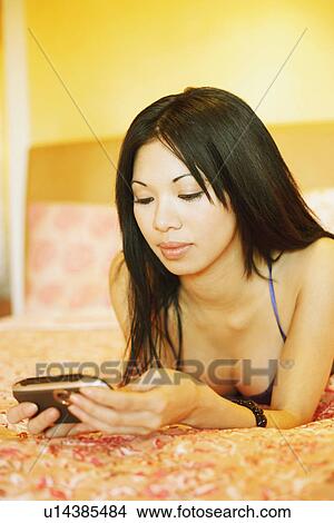Close-up of a young woman lying on the bed and using a mobile phone View Large Photo Image Picture - Close-up of a young woman lying on the bed and using a mobile phone. Fotosearch