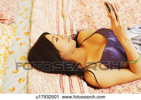 High angle view of a young woman lying on the bed and using a mobile phone View Large Photo Image Stock Image - High angle view of a young woman lying on the bed and using a mobile phone. Fotosearch