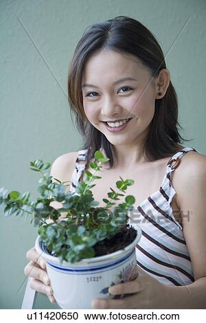 Portrait of a young woman holding a potted plant and smiling View Large Photo Image Stock Image - Portrait of a young woman holding a potted plant and smiling. Fotosearch