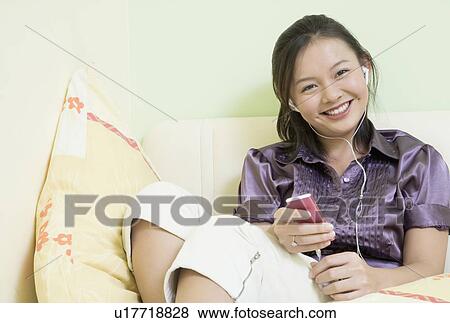 Portrait of a young woman leaning against a wall and listening to music View Large Photo Image Stock Photo - Portrait of a young woman leaning against a wall and listening to music. Fotosearch
