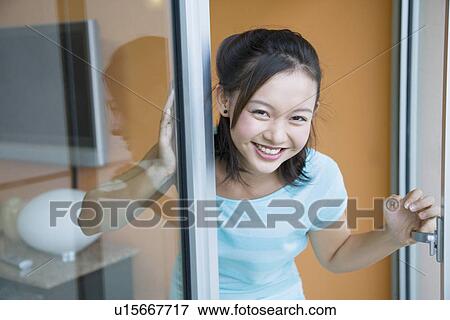 Stock Photo - Portrait of a young woman looking out of a door. Fotosearch