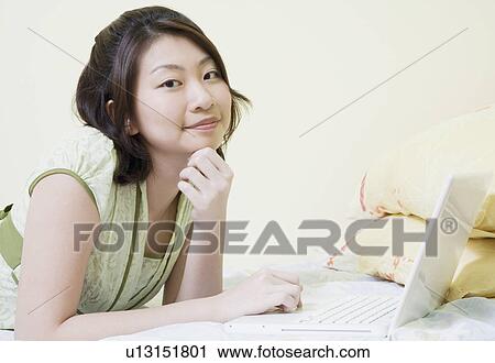 Portrait of a young woman lying on the bed and using a laptop View Large Photo Image Stock Image - Portrait of a young woman lying on the bed and using a laptop. Fotosearch