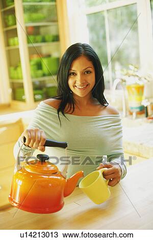 Stock Image - Portrait of a young woman pouring tea into a tea cup. Fotosearch