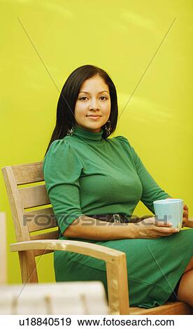Portrait of a young woman sitting in an armchair and holding a tea cup View Large Photo Image Stock Photo - Portrait of a young woman sitting in an armchair and holding a tea cup. Fotosearch