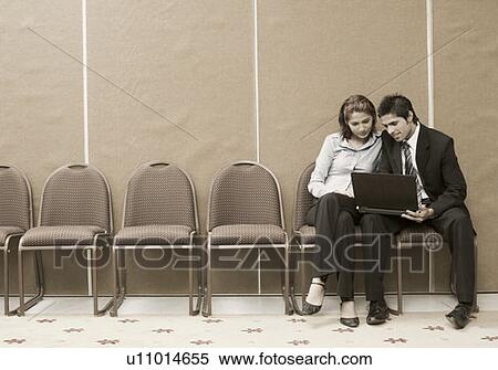 Stock Photography - Businessman sitting with a businesswoman and using a laptop. Fotosearch