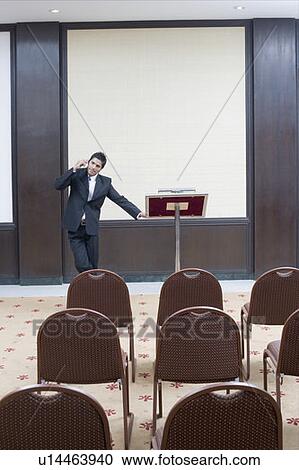 Businessman standing at a lectern and talking on a mobile phone View Large Photo Image Stock Image - Businessman standing at a lectern and talking on a mobile phone. Fotosearch