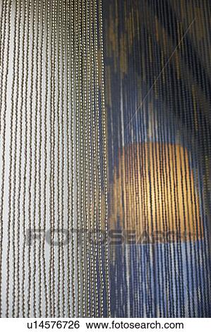 Stock Photograph - Close-up of a beaded curtain with a lampshade lit in the background. Fotosearch
