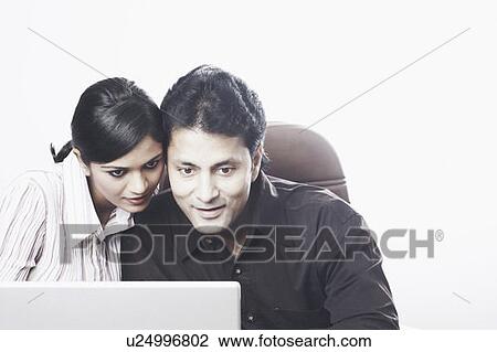 Stock Image - Close-up of a businessman and a businesswoman working on a laptop. Fotosearch