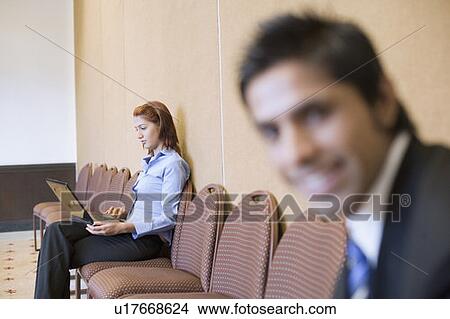 Picture - Close-up of a businessman smiling with a businesswoman using a laptop in the background. Fotosearch