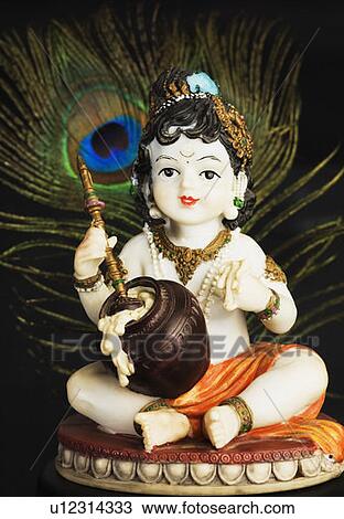Stock Image - Close-up of a figurine of God Krishna with a peacock feather. Fotosearch