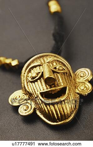 Stock Image - Close-up of a human face shaped golden pendant. Fotosearch