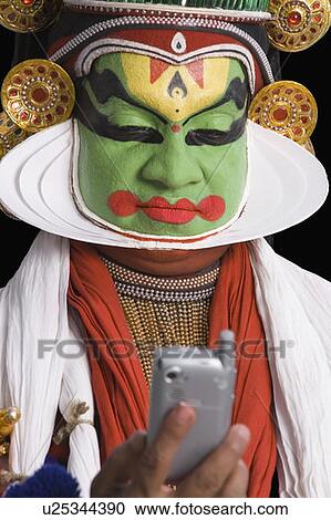 Stock Image - Close-up of a Kathakali dance performer holding a mobile phone. Fotosearch